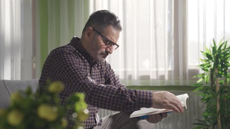 Mature-man-with-glasses-is-reading-a-book-at-home.